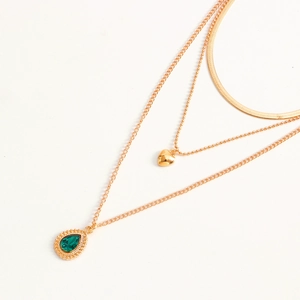Detailopname van drielaagse gouden ketting met groene druppel edelsteen en hartvormige hanger