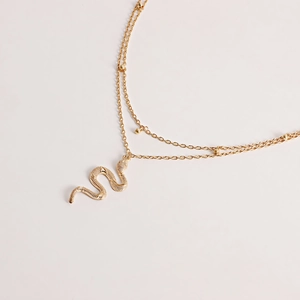 Détail d'un collier doré double épaisseur avec pendentif serpent et perles délicates