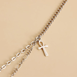 Macro detail of silver Ankh cross pendant with layered Figaro and Cuban chain link style