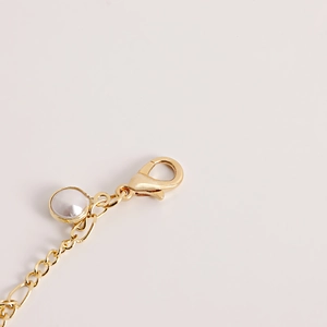 Detailed macro shot of a golden lobster clasp with a white pearl charm on a metal chain