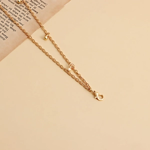 Détail d'une chaîne de taille dorée à double rangée avec perles et fermoir mousqueton