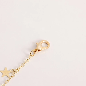 Macro detail of gold metal waist chain featuring a lobster clasp and star charm pendant
