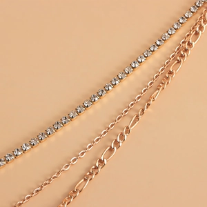 Layered gold chain set featuring crystal tennis chain and Figaro links on beige background