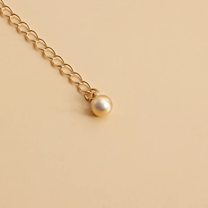 Detail of a golden metal waist chain with a delicate champagne pearl pendant at the end