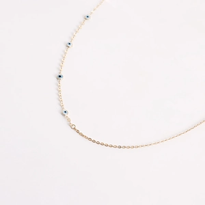 Detailed close-up of golden metal chain with blue evil eye charms on white background
