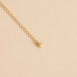 Close-up of golden link chain with a glossy faux pearl pendant on a minimalist background