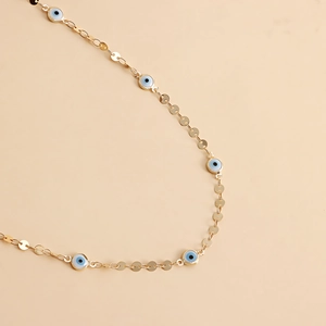 Detail of gold chain belt featuring blue evil eye charms and polished metal discs