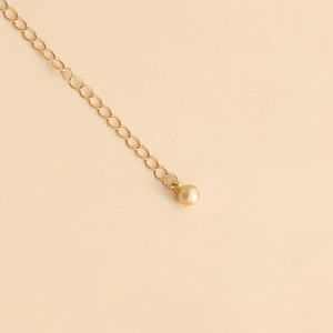 Close-up of golden waist chain featuring a polished metal link and a light gold pearl drop