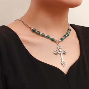 Macro view of vintage silver cross pendant with emerald green beads on layered necklace
