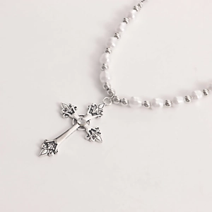 Close-up of gothic silver cross pendant with central zircon and white pearl strand necklace