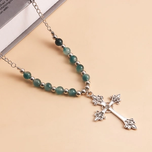 Close-up of vintage silver cross pendant with emerald green beads and sparkling zircon
