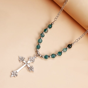 Close-up of vintage hollow cross pendant with green beads and silver chain link