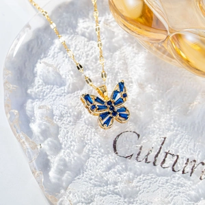 Close-up of butterfly necklace with blue rectangle stones on a glass tray
