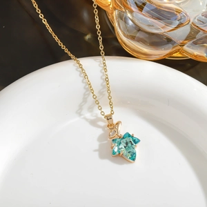 Detail shot of a vintage gold maple leaf pendant necklace with blue crystal and zircon in a bowl