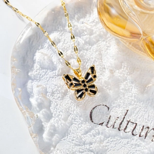 Detail of gold butterfly necklace with black stones on textured white plate