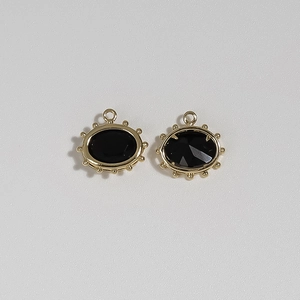 Detail of two oval gold-plated Evil Eye pendants with black stone and beaded edges