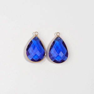 Close-up of teardrop shaped dark blue crystal pendants with gold metal edge for DIY jewelry