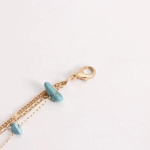 Détail de la chaîne dorée multicouche avec perles turquoise et fermoir mousqueton