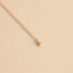 Detailed close-up of golden metal chain link with a polished round bead pendant detail