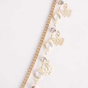Detailed macro view of gold butterfly pendants and clear crystals on a layered metal chain