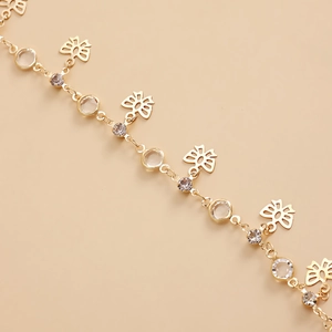 Detail of gold chain with hollow flower pendants and inlaid crystals on beige background