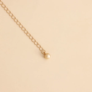 Detail showing the gold metal extension chain with a round champagne pearl pendant