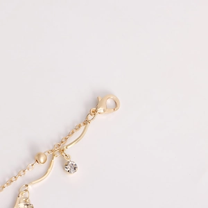 Macro detail of gold body chain featuring a lobster clasp and a round zircon pendant