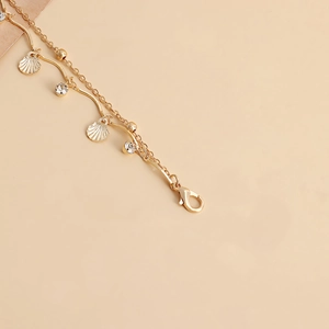 Detail of a double-layered gold body chain featuring a scallop charm and zircon accents