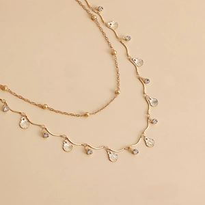 Detail of gold layered body chain with shell pendant and zircon stones on beige background