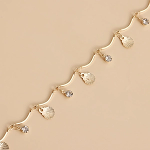 Detail of gold body chain featuring wave links, seashell charms, and sparkling zircons