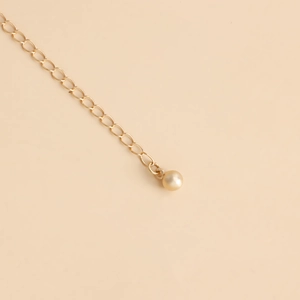Macro shot of gold body chain with elegant champagne faux pearl pendant detail