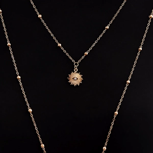 Detalle de collares dorados en capas con colgante de sol y ojo sobre fondo negro