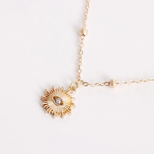 Detalle de cadena corporal dorada con colgante de sol y ojo con incrustación de circón blanco