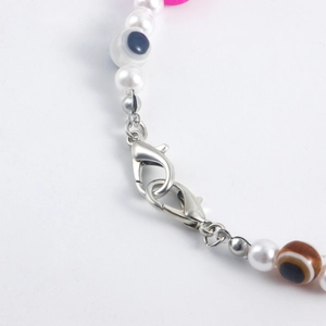 Detailed macro view of beaded anklet with white pearls, evil eye charms, and lobster clasps