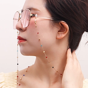 Détail d'une chaîne de lunettes dorée avec perles colorées portée par un mannequin en gros plan