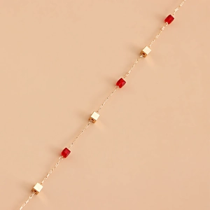 Détail d'une chaîne à lunettes dorée avec perles rouges rectangulaires et carrées