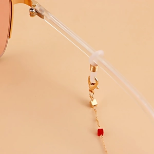 Détail de la chaîne de lunettes dorée avec perle rouge et breloque sur boucle silicone