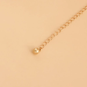 Détail d'une chaîne de corps dorée multicouche avec un petit pendentif en boule