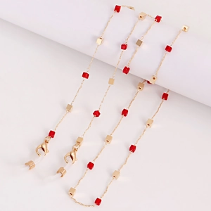 Détail macro de la chaîne de lunettes dorée avec perles de cristal rouge sur fond blanc