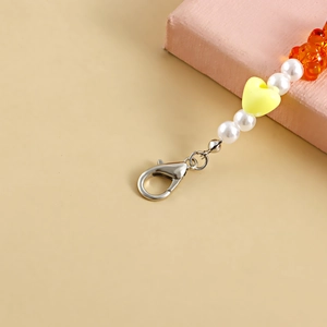 Detail of beaded shoe charm featuring white pearls, yellow heart, and orange resin bear