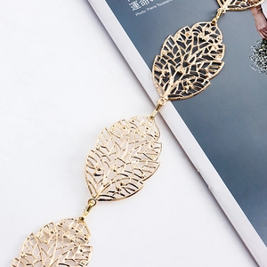 Détail de la chaîne de taille en métal doré avec feuilles ajourées sur un fond de magazine