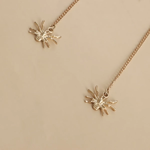 Detailed macro view of golden spider drop earrings with long metallic chains