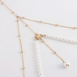 Macro shot of gold chain leg ring with white pearl charms and floral metal connector
