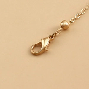 Macro detail of matte gold lobster clasp with decorative bead and link chain extension