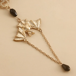 Detail of golden bat pendant with black faceted beads and double chain on beige background