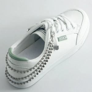 White sneakers with layered rhinestone chain and fashion label on clean grey background