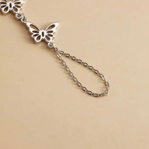 Makro-Detail einer silbernen Schmetterling-Handkette mit hohlen Anhängern und Ring