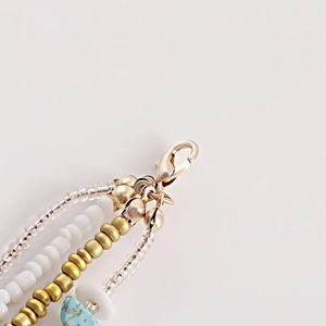 Detail view of bohemian body chain with gold bells, white beads, and turquoise stone