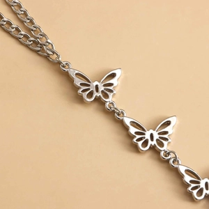 Makroaufnahme einer silbernen Metallkette mit hohl gearbeiteten Schmetterlingsanhängern und Gliedern