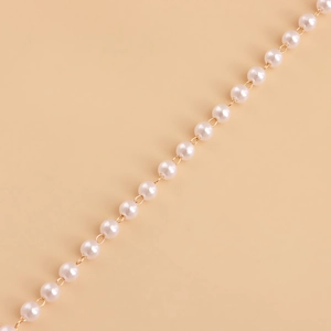 Macro detail of double-layer faux pearl waist chain with golden metal link fasteners